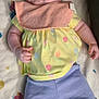 baby, child, smiling, yellow_shirt, purple_pants, bib, blanket, patterned_blanket, lying_down, happy, infant, cute, soft_lighting, indoors, person, small_hands, pink_socks, face, cheerful, toddler