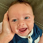 Luca James is registered to the contest to win money with this photo: baby, smiling, face, hand, clothing, blue_shirt, infant, portrait, cute, happy, skin, eyes, mouth, person, closeup, child, seated, fabric, stitching, casual