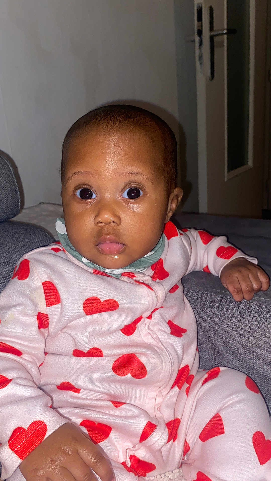 Jessica a rejoint le concours — aidez-le/la à gagner de superbes lots ! baby, infant, child, onesie, heart_pattern, pajamas, couch, living_room, face, wide_eyes, surprised_expression, sitting, hand, flash_photography, indoor, door, pillow, skin_tone, portrait, clothing