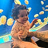 Javier is registered to the contest to win money with this photo: adult_arms, aquarium, baby, blue_background, child, curly_hair, family, infant, jellyfish, marine_life, outdoor_like, peach_shirt, photography, portrait, reaching, sitting, smiling, supported, tattoo, underwater