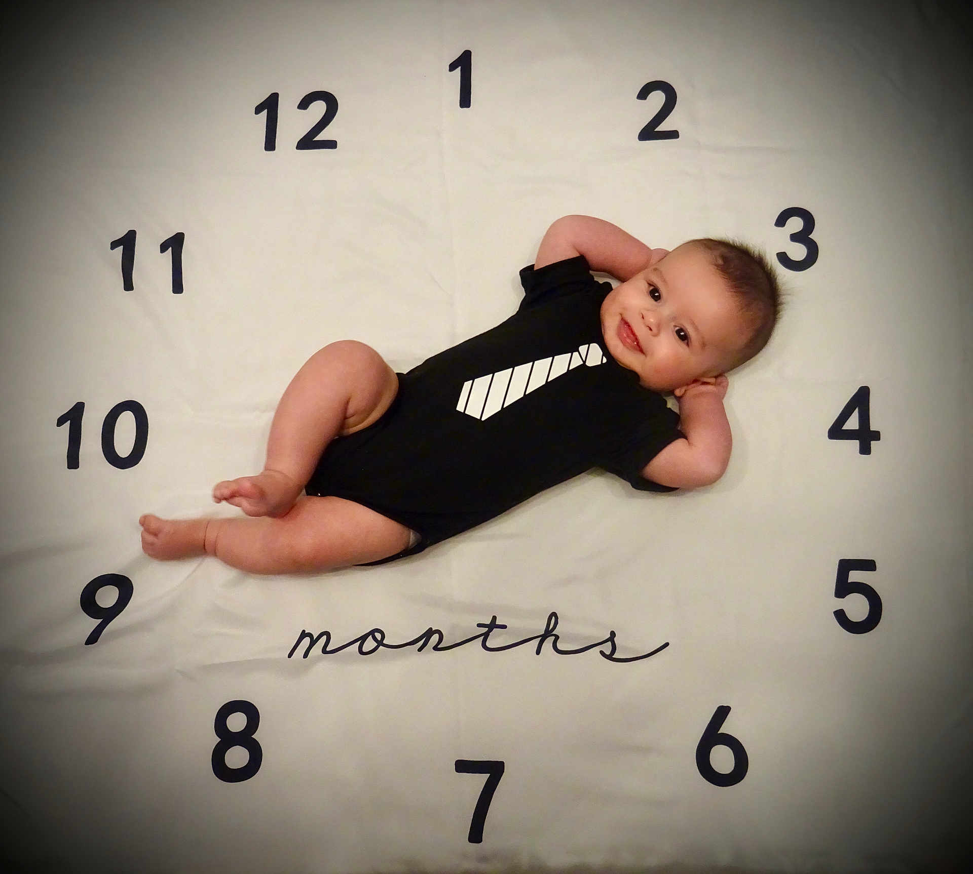 Soren participe au concours pour gagner de l'argent avec cette photo : baby, infant, child, milestone_blanket, numbers, months, clock_layout, onesie, tie_print, smile, lying_down, portrait, vignette, soft_lighting, cute, hands_up, bare_feet, background, nursery, photography