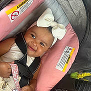Ava is registered to the contest to win money with this photo: baby, child, smiling, headband, bow, car_seat, safety_harness, pink, gray, pacifier, hand, clothing, cute, infant, seat, happy, person, indoor, closeup, transportation