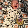baby, smiling, infant, patterned_blanket, white_clothing, black_bows, wooden_sign, months, happy, lying_down, portrait, child, cute, cheerful, indoor, person, small_hands, small_feet, face, expression