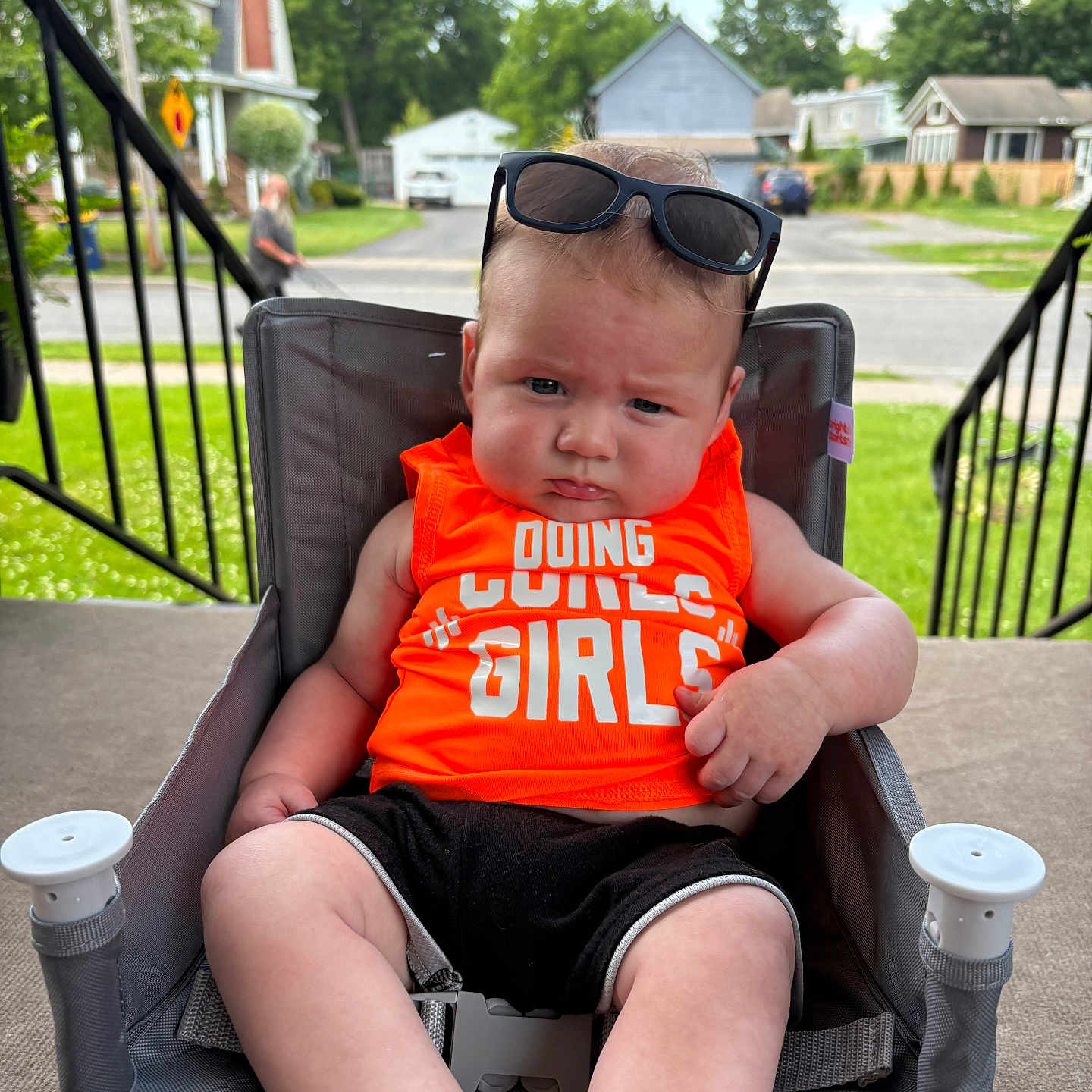 Sawyer joined the competition — help win amazing prizes! baby, child, sunglasses, orange_shirt, chair, outdoor, porch, street, residential_area, grass, person, summer, clothing, footwear, expression, face, headwear, sunlight, furniture, casual