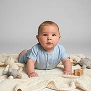 Issaiah Lebron joined the competition — help win amazing prizes! baby, child, infant, blue_clothing, blanket, knitted, plush_toys, wooden_toy, star_shaped_toy, cute, portrait, laying_down, indoors, soft_lighting, adorable, curious, face, hand, floor, studio