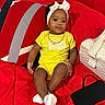 baby, child, yellow_clothing, headband, red_couch, pillow, quilted_bag, smartphone, sitting, indoors, cute, portrait, accessories, bracelet, white_socks, infant, happy, comfortable, modern, relaxed