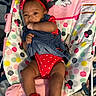 baby, infant, child, red_headband, red_clothing, denim_overalls, baby_chair, minnie_mouse, polka_dots, colorful, cute, chewing_hand, sitting, indoor, portrait, smiling, red_booties, young_child, playful, expression