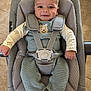 baby, smiling, infant, knitted_clothing, baby_seat, safety_harness, face, head, hands, socks, floor, tile, cute, indoors, child, person, happy, seated, cozy, comfortable