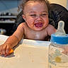 Karmelo is registered to the contest to win money with this photo: baby, high_chair, curly_hair, laughing, messy_face, food, hand, bottle, table, infant, child, smile, indoor, feeding, cute, happy, young, skin, tongue, meal