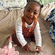 Leia joined the competition — help win amazing prizes! baby, child, smiling, pigtails, sock, bed, blanket, stuffed_animal, toy, pink, white_clothing, orange_overall, happy, indoors, cute, portrait, toddler, sitting, soft_toy, cozy