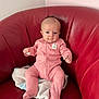 baby, infant, pink_onesie, red_chair, towel, seated, indoor, cute, small_hands, small_feet, curious_expression, soft_lighting, head, face, person, child, furniture, comfortable, portrait, casual