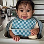 Cyrus joined the competition — help win amazing prizes! baby, child, high_chair, bib, smile, hair, pony_tail, bottle, hand, face, indoor, living_room, stairs, window, furniture, person, happy, cute, portrait, checkered_pattern