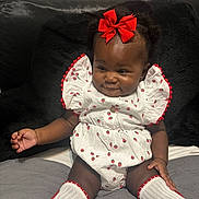 Robyn Joy is registered to the contest to win money with this photo: baby, bed, black_pillow, child, clothing, cute, happy, headboard, indoor, infant, knee_high_socks, person, pillow, portrait, red_bow, red_trim, sitting, smiling, strawberry_pattern, white_outfit