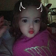 Macelynn is registered to the contest to win money with this photo: child, toddler, portrait, indoors, sitting, pink_shirt, curly_hair, dark_hair, facial_expression, pursed_lips, doodle, horns, bedroom, couch, blanket, arm, close_up, low_light, grainy, family