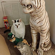 Chewy joined the competition — help win amazing prizes! animal_figure, black_markings, carpet, cat, curious, decor, feline, floor, gray_statue, home, indoor, orange_statue, room, sculpture, sitting, statue, tiger_statue, vent, wall, white_cat