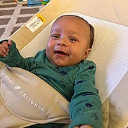 Keena is registered to the contest to win money with this photo: baby, baby_delight, baby_seat, carpet, child, cushion, fabric, face, green_clothing, hand, happy, home, indoor, infant, living_room, onesie, person, seat, smile, toy