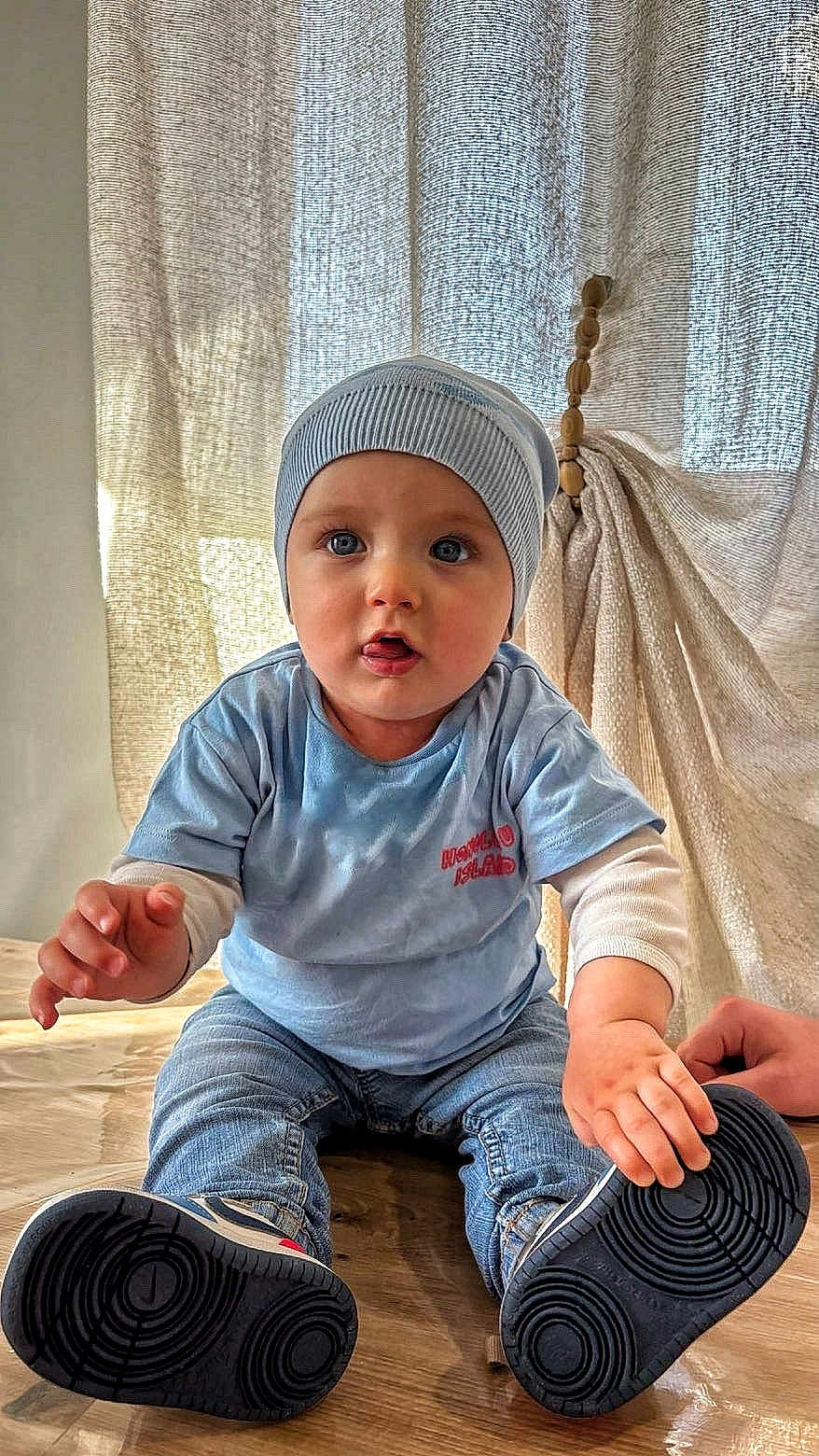 Santiano participe au concours pour gagner de l'argent avec cette photo : baby, child, blue_shirt, blue_beanie, jeans, shoe, floor, curtain, indoor, cute, sitting, hand, footwear, light, texture, person, portrait, young_child, casual_clothing, expression