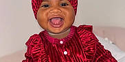 Thaissya participe au concours pour gagner de l'argent avec cette photo : baby, child, cute, expression, face, fashion, hand, happy, headwrap, indoors, infant, musical_notes, pillow, portrait, red_clothing, sitting, smiling, soft_fabric, texture, warm_lighting
