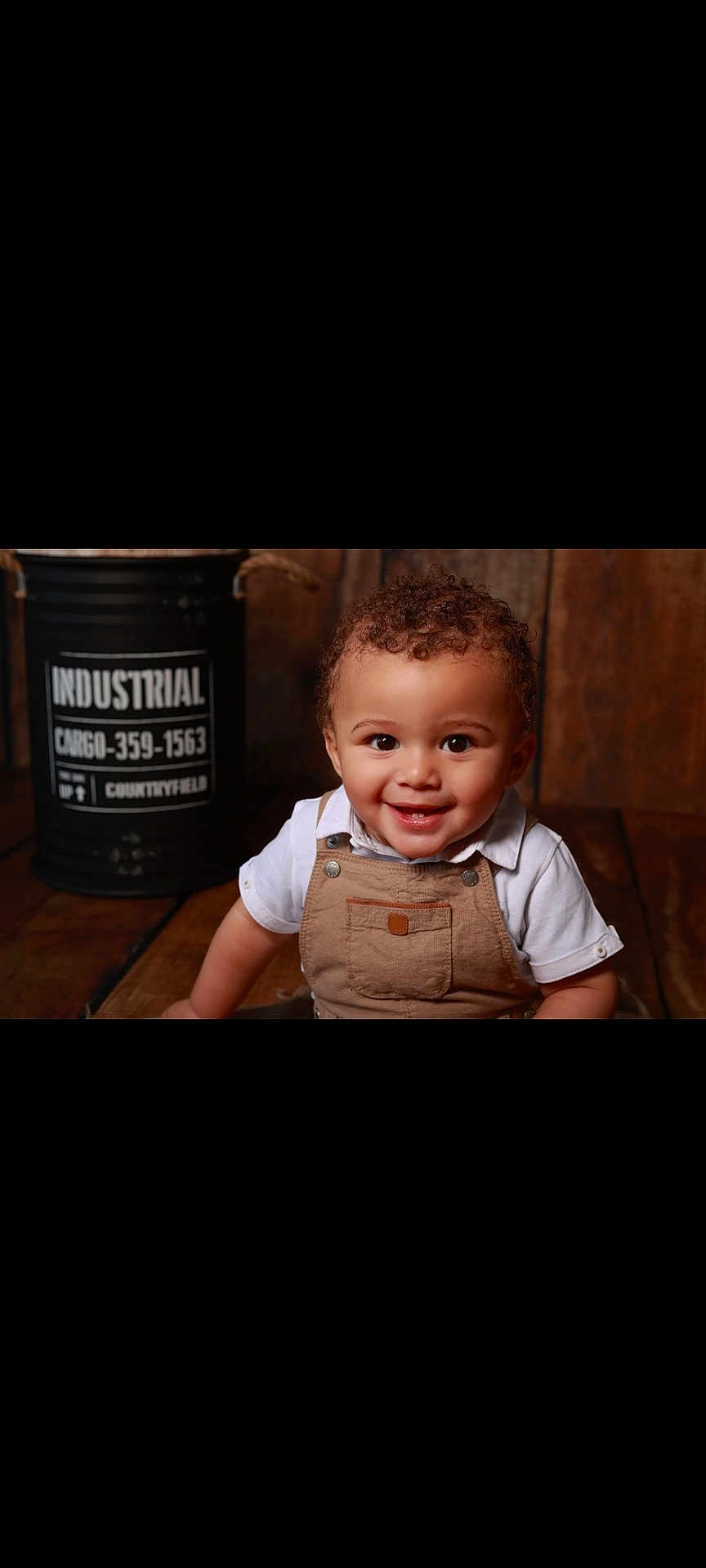 Lucas a rejoint le concours — aidez-le/la à gagner de superbes lots ! toddler, child, smiling, curly_hair, overalls, white_shirt, wooden_floor, indoor, barrel, industrial, portrait, happy, cute, person, baby, sitting, face, eyes, background, rustic