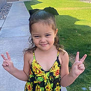 Aleyah is registered to the contest to win money with this photo: child, girl, smiling, peace_sign, sunflower_dress, black_bow, outdoor, sidewalk, grass, residential_area, happy, person, curly_hair, summer, casual_clothing, nature, portrait, young, cute, daylight
