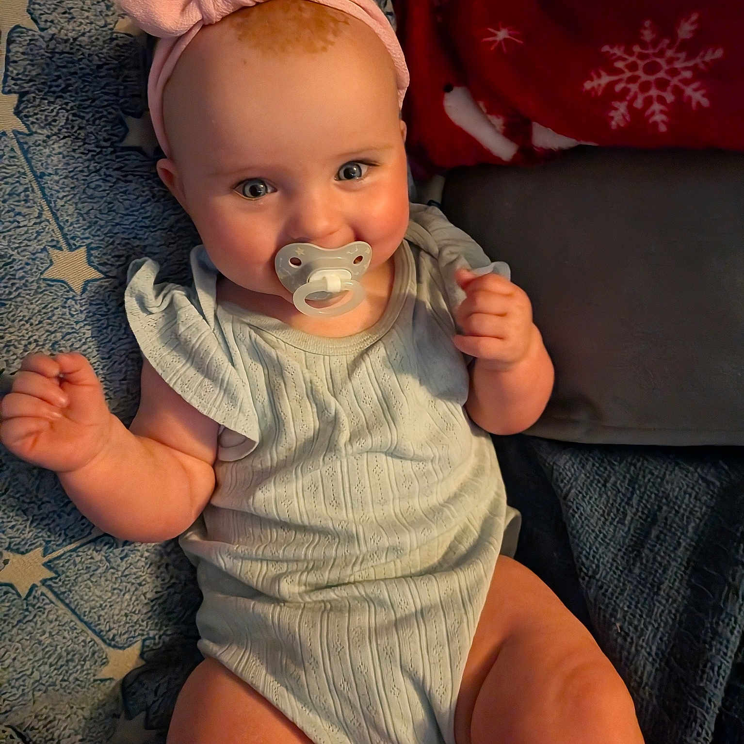 Joy is registered to the contest to win money with this photo: baby, pacifier, headband, blanket, star_pattern, red_blanket, infant, smile, cute, chubby_cheeks, clothing, sitting, person, skin, hand, legs, face, indoors, portrait, soft_texture
