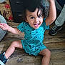 toddler, child, smiling, sitting, turquoise_outfit, dinosaur_print, black_sneakers, hat, wooden_floor, indoor, happy, person, footwear, toy, playful, motion_blur, hand, face, hair, adult_leg
