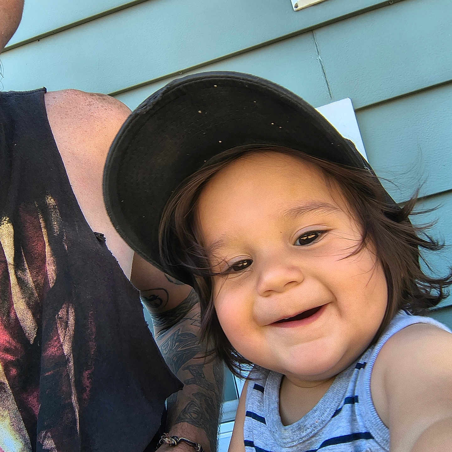 Walter joined the competition — help win amazing prizes! adult, arm, blue_wall, bracelet, cap, casual, child, closeup, face, hair, happy, outdoor, person, selfie, smiling, striped_clothing, sunlight, tank_top, tattoo, toddler