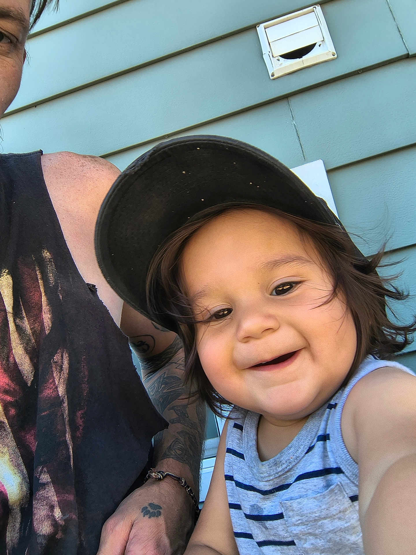 Walter joined the competition — help win amazing prizes! child, toddler, smiling, cap, striped_clothing, tank_top, selfie, tattoo, adult, arm, bracelet, outdoor, blue_wall, hair, face, happy, person, closeup, casual, sunlight