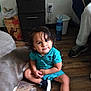 Walter is registered to the contest to win money with this photo: toddler, child, dog, floor, wooden_floor, sitting, wet_hair, turquoise_clothing, black_shoes, water_bottle, drawer, plastic_bin, person, leg, shoe, indoor, curious_expression, pet, home, casual