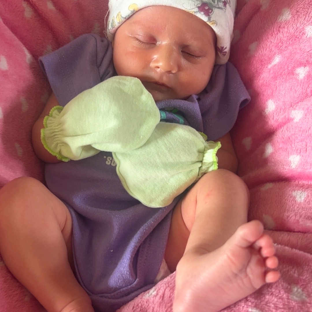 Elena is registered to the contest to win money with this photo: baby, newborn, infant, sleeping, hat, mittens, blanket, pink, purple_clothing, feet, toes, soft_texture, cute, peaceful, resting, person, indoors, cozy, headwear, closeup