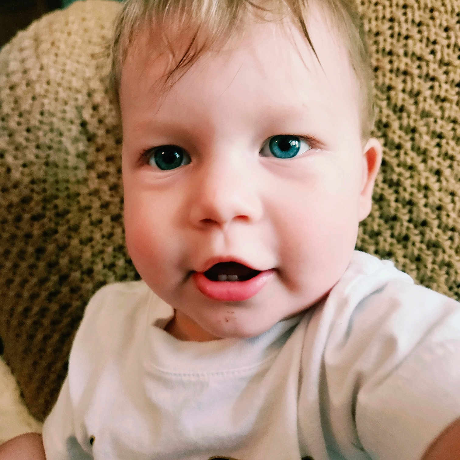 Beckham is registered to the contest to win money with this photo: baby, background, blue_eyes, child, close_up, curly_hair, cute, expression, face, head, indoor, mouth, person, portrait, sitting, skin, smiling, texture, white_shirt, young