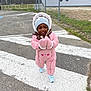Aissata a rejoint le concours — aidez-le/la à gagner de superbes lots ! child, toddler, pink_snowsuit, beanie, mittens, sneakers, crosswalk, outdoor, fence, sports_field, asphalt, winter_clothing, smiling, walking, cold_weather, grass, trees, daytime, person, happy
