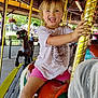 Penelope joined the competition — help win amazing prizes! child, smiling, carousel, amusement_park, horse, ride, golden_pole, outdoor, daylight, fun, playful, pink_shorts, white_shirt, happy, person, wooden_roof, string_lights, people, background, fence