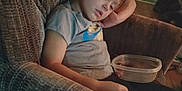 Penelope is registered to the contest to win money with this photo: child, sleeping, armchair, plastic_container, indoor, casual_clothing, toddler, relaxed, home, furniture, young_child, resting, peaceful, curly_hair, closed_eyes, seated, dim_lighting, carpet, floor, cozy