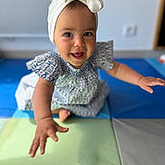 Zeyna participe au concours pour gagner de l'argent avec cette photo : baby, child, girl, smiling, reaching, headband, bow, dress, patterned_clothing, play_mat, indoor, happy, cute, portrait, closeup, person, skin, arm, foot, floor