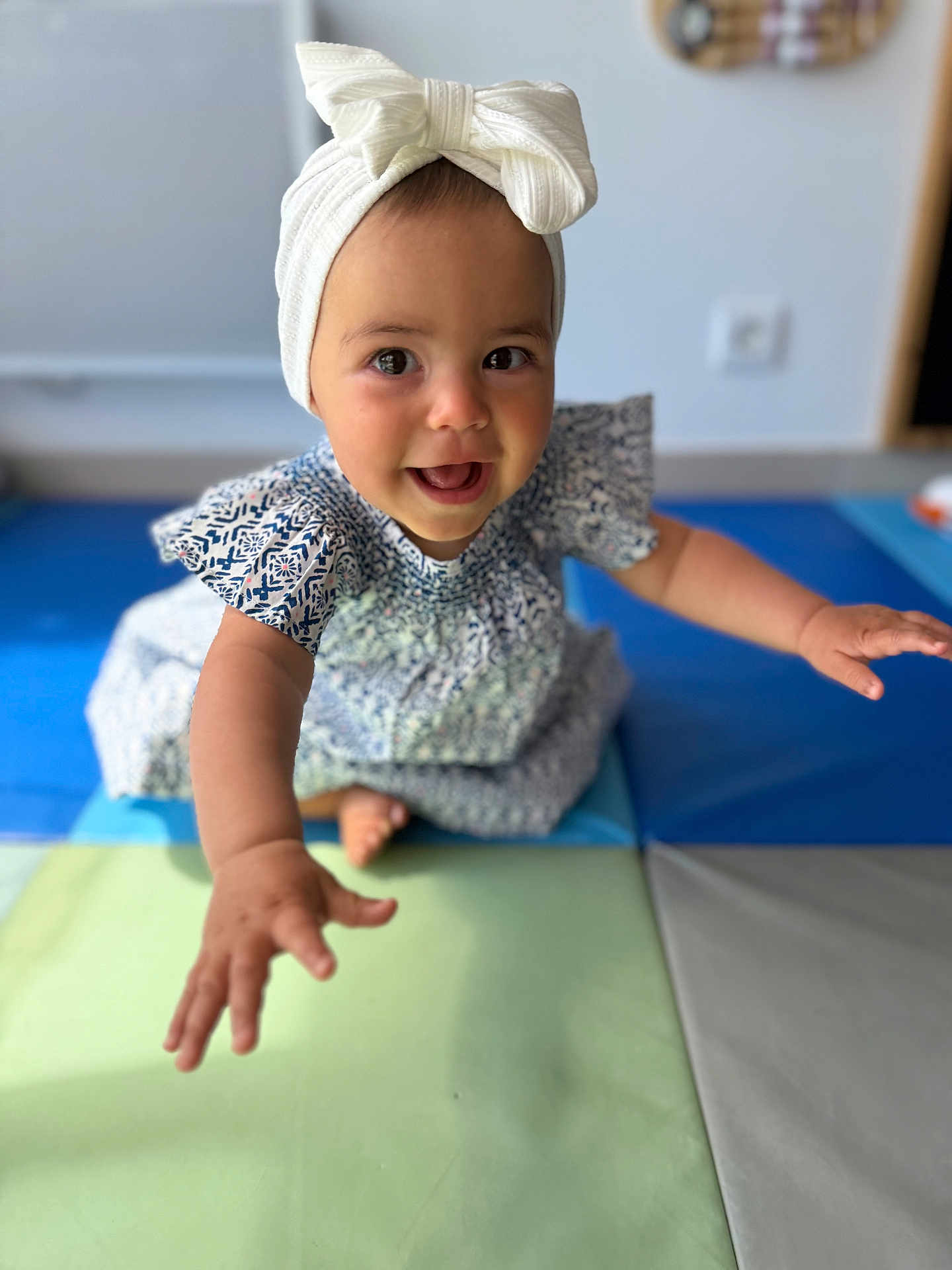 Zeyna participe au concours pour gagner de l'argent avec cette photo : baby, child, girl, smiling, reaching, headband, bow, dress, patterned_clothing, play_mat, indoor, happy, cute, portrait, closeup, person, skin, arm, foot, floor