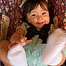 baby, child, smiling, headband, socks, car_seat, floral_pattern, cute, happy, infant, clothing, toddler, playful, face, person, young_child, indoors, portrait, seatbelt, colorful