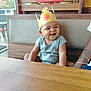 toddler, child, burger_king, crown, smile, happy, restaurant, booth, wood, cushion, window, daylight, casual_clothing, person, indoor, portrait, cute, seated, fun, cheerful