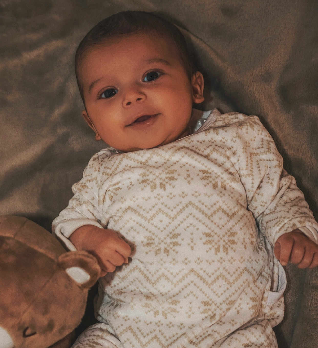 Kemys participe au concours pour gagner de l'argent avec cette photo : baby, infant, smiling, onesie, blanket, plush_toy, teddy_bear, cozy, cute, child, portrait, indoors, soft_lighting, happy, lying_down, patterned_clothing, young, peaceful, closeup, warm