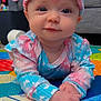 baby, infant, child, headband, tie_dye, colorful, play_mat, hands, face, eyes, indoor, couch, pillow, soft_toys, clothing, smile, cute, portrait, home, floor