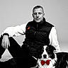 man, person, dog, border_collie, bow_tie, black_and_white, portrait, studio, fashion, formalwear, sitting, lying_down, pet, animal, companion, white_background, high_contrast, red_accent, outdoorless, photography