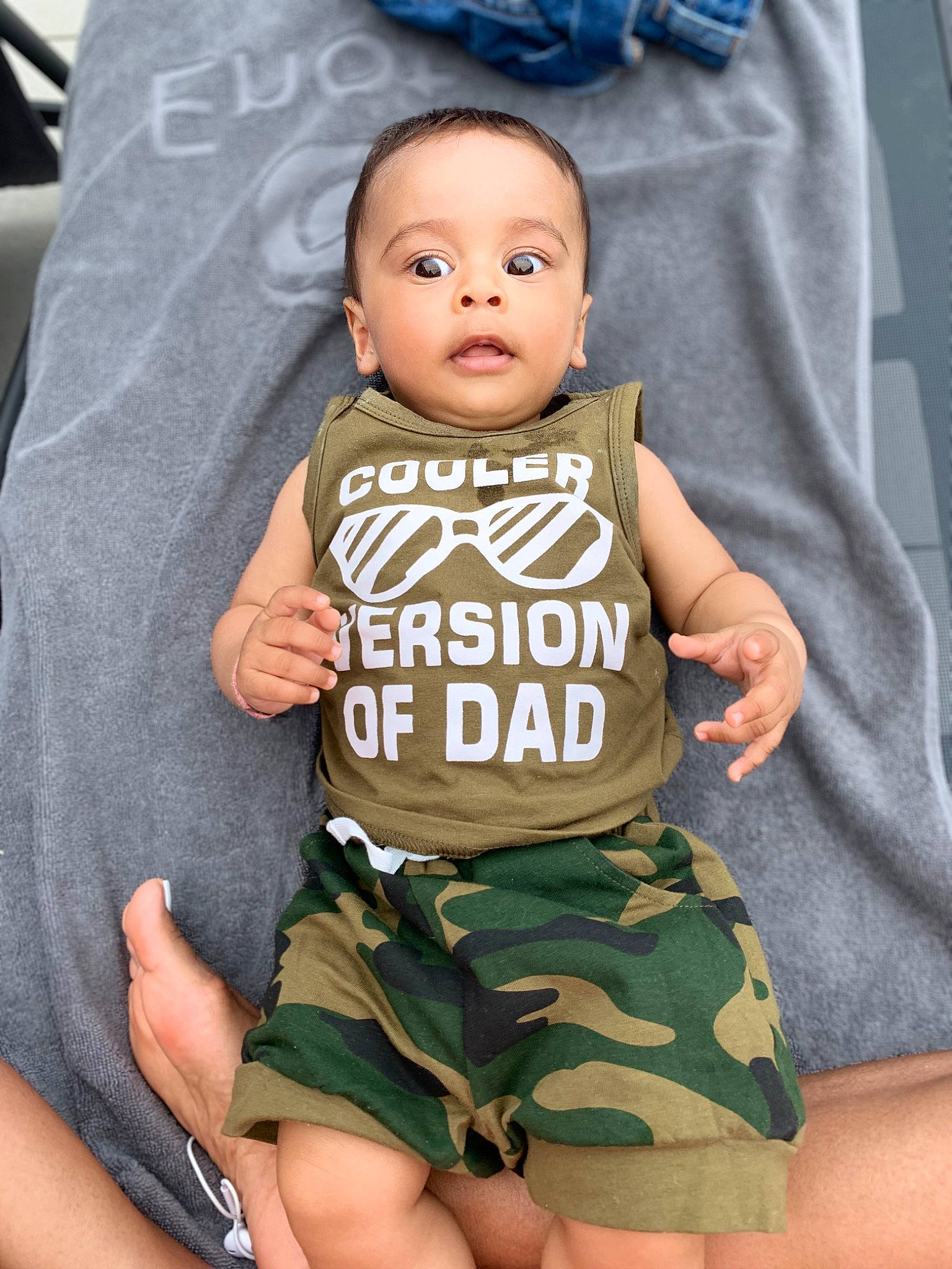 Kian is registered to the contest to win money with this photo: arm, baby, baby_toddler_clothing, blue, cheek, eye, finger, gesture, hand, happy, head, human_body, joint, neck, outerwear, person, skin, sleeve, t_shirt, thigh