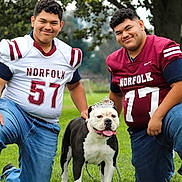 Princess is registered to the contest to win money with this photo: bulldog, dog, football, football_players, sports_jerseys, team_portrait, outdoor, park, grass, family, two_people, smiling, crown, pet, athlete, sports, uniform, portrait, trees, daylight