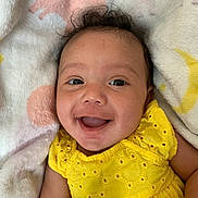 Joi is registered to the contest to win money with this photo: adorable, baby, blanket, cheerful, child, closeup, clothing, cute, face, happy, head, indoor, infant, lying_down, person, portrait, smiling, soft_texture, yellow_dress, young_child
