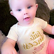 Mia is registered to the contest to win money with this photo: baby, child, infant, face, smile, headband, flower, blue_eyes, couch, pillow, clothing, white_shirt, pink_pants, toddler, sitting, cute, indoors, person, happy, portrait