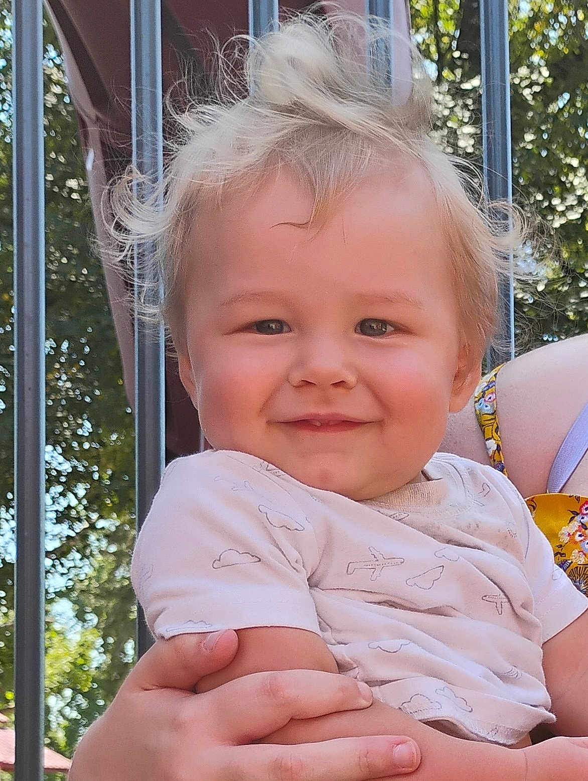 Aiden joined the competition — help win amazing prizes! toddler, child, smile, blonde_hair, outdoor, sunlight, trees, metal_bars, holding, person, happy, cute, baby_clothes, short_sleeves, face, portrait, nature, daylight, parent, hand