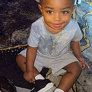 Amor is registered to the contest to win money with this photo: toddler, child, smile, braided_hair, gray_outfit, black_sneakers, sitting, carpet, floor, indoor, person, young_child, cute, happy, necklace, portrait, casual_clothing, playful, home, flooring