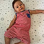 baby, infant, child, crib, striped_clothing, red_and_white, blue_pocket, smiling, lying_down, star_pattern, moon_pattern, sun_pattern, bed_sheet, cute, relaxed, happy, indoors, portrait, skin, person