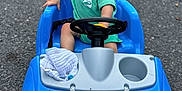 Easton joined the competition — help win amazing prizes! toddler, child, toy_car, blue, green_shirt, steering_wheel, outdoor, asphalt, happy, smiling, short_hair, sitting, play, vehicle, plastic, wheel, daylight, expression, cute, small