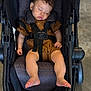 baby, sleeping, stroller, infant, child, brown_outfit, footwearless, seatbelt, relaxed, indoor, cute, peaceful, toddler, headrest, soft_lighting, black_stroller, small_child, hands, legs, nap